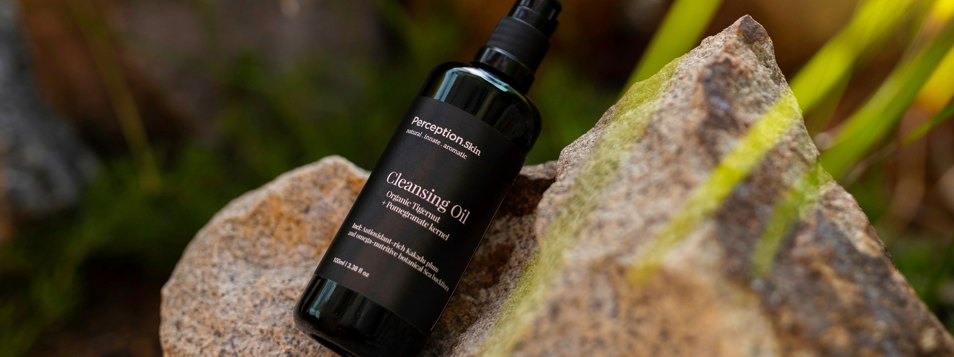 Perception Skin Cleansing Oil resting on a textured rock with a blurred natural outdoor background.