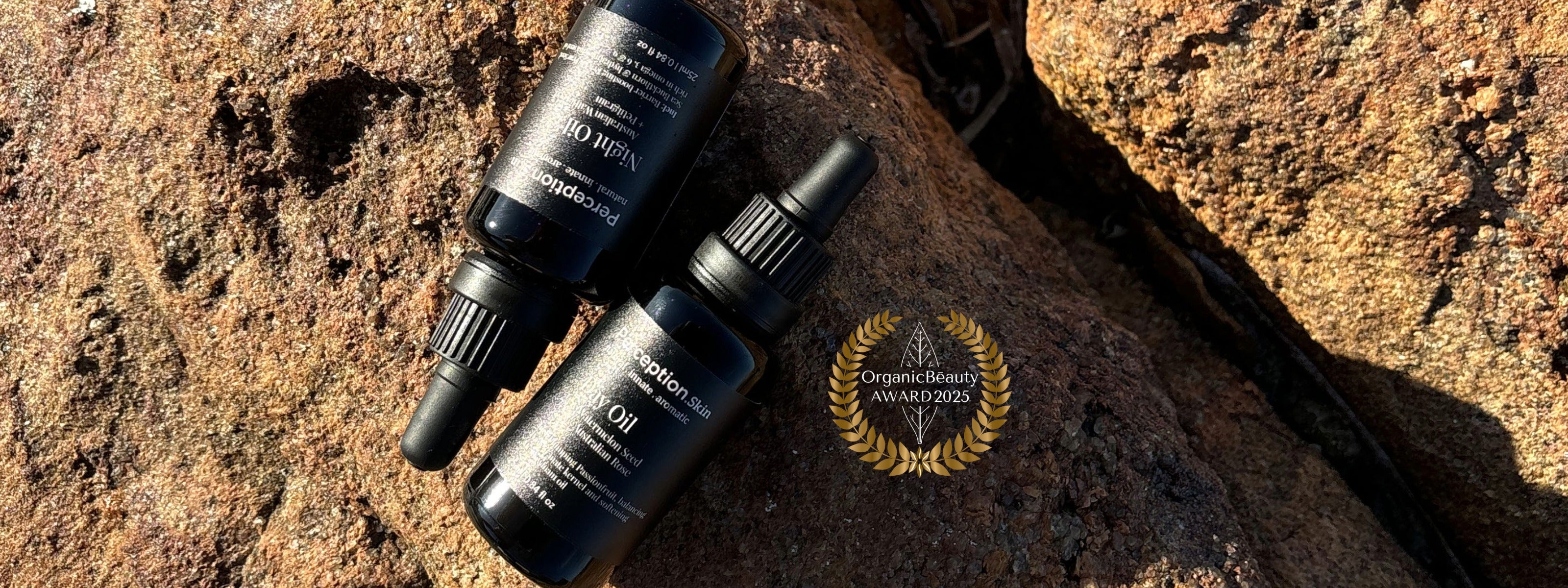 Perception Skin Day + Night Oils placed on a rock with Organic Beauty Awards badge