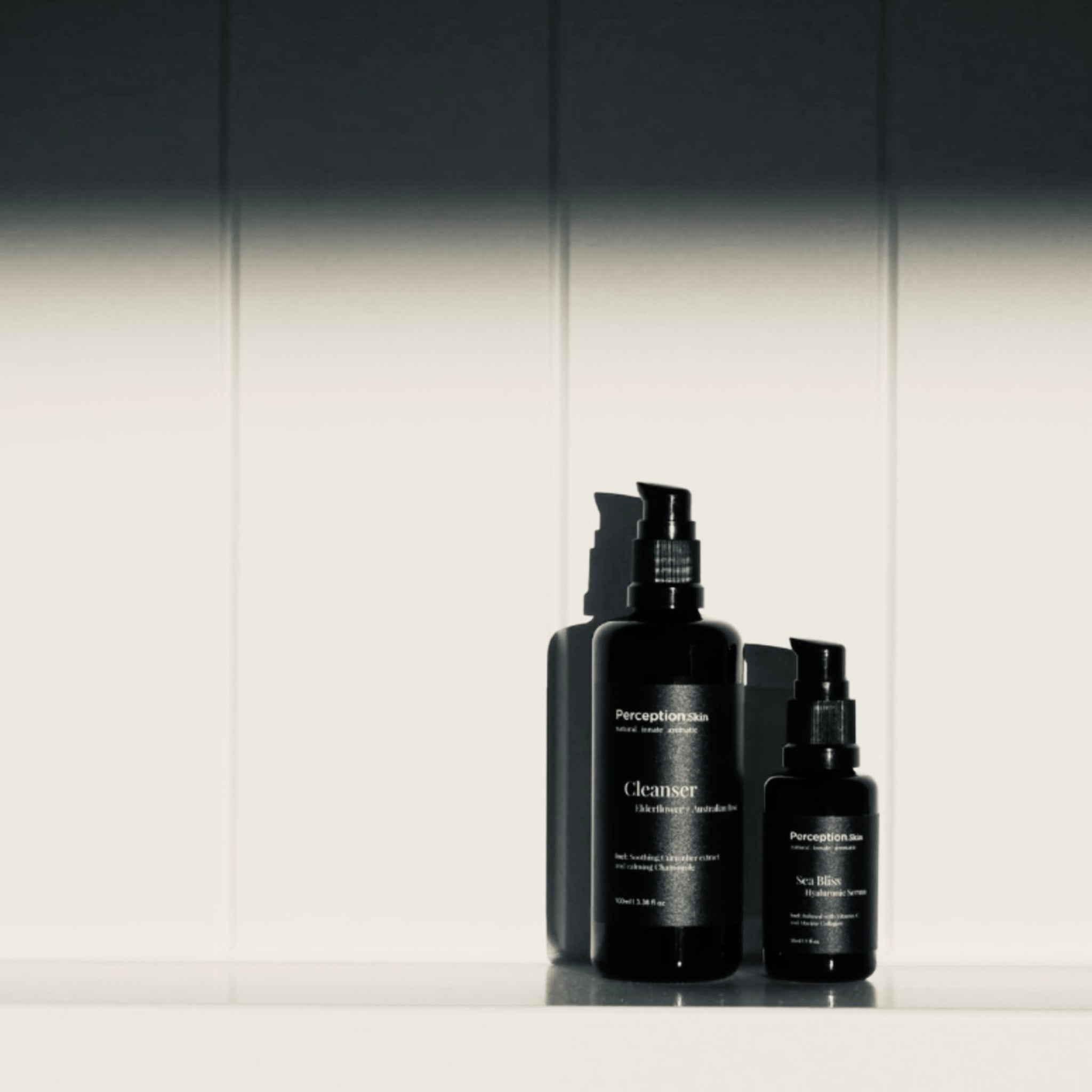 Perception Skin Australian Rose Cleanser + Sea Bliss Hyaluronic Serum on a white board with a wooden white backdrop background