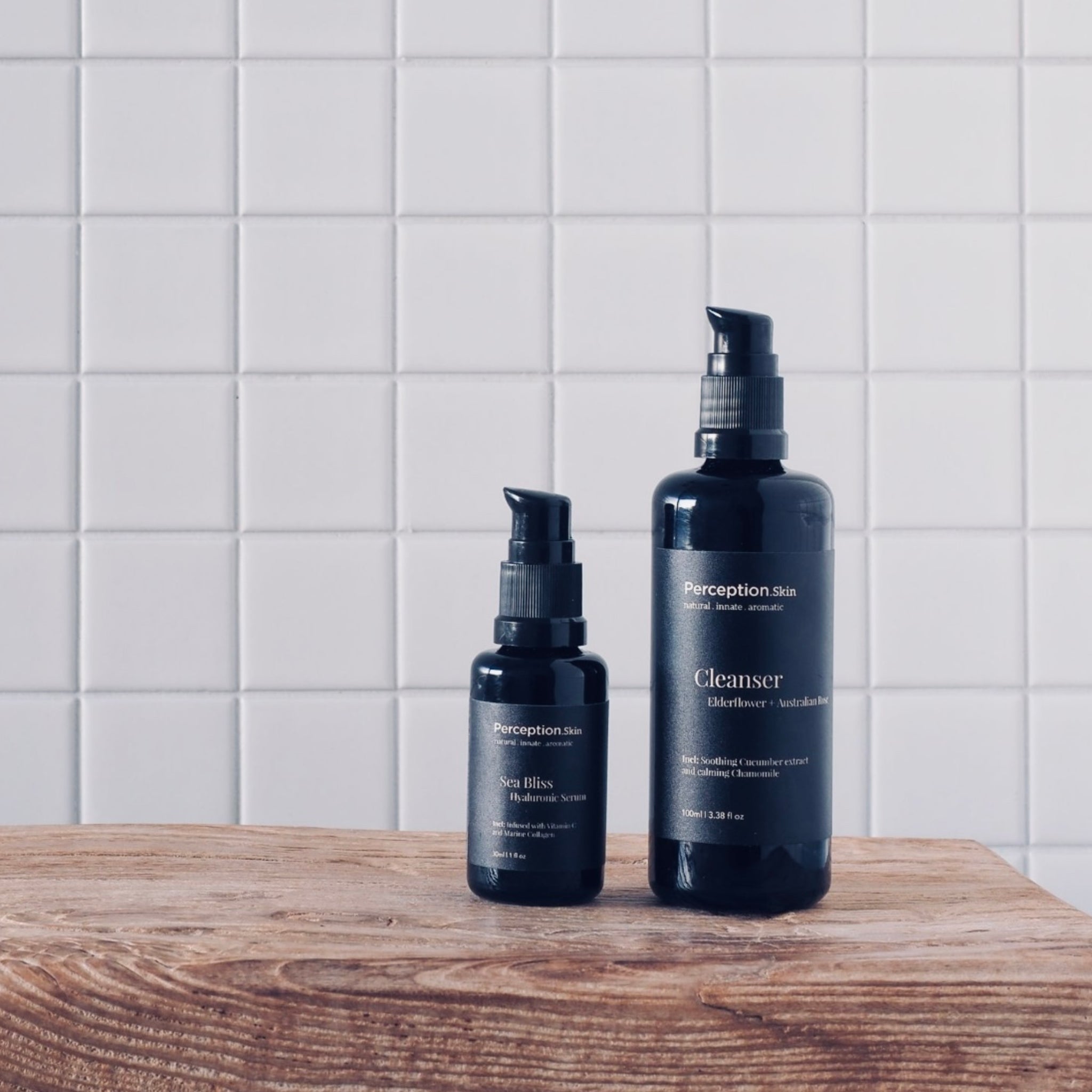 Perception Skin Australian Rose Cleanser + Sea Bliss Hyaluronic Serum on a wooden surface with a white tile background