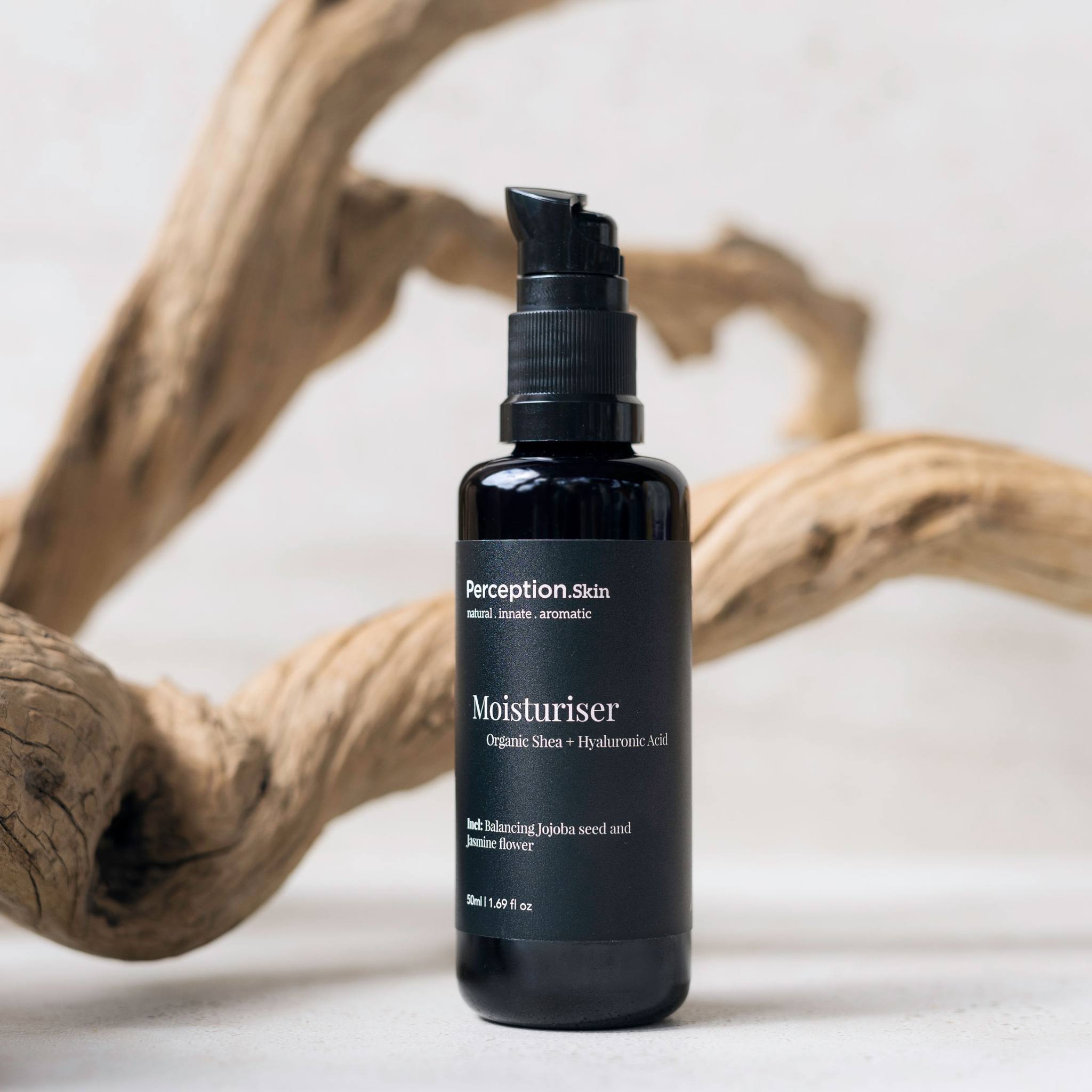 Black bottle of Perception Skins Moisturiser on a neutral background with driftwood.