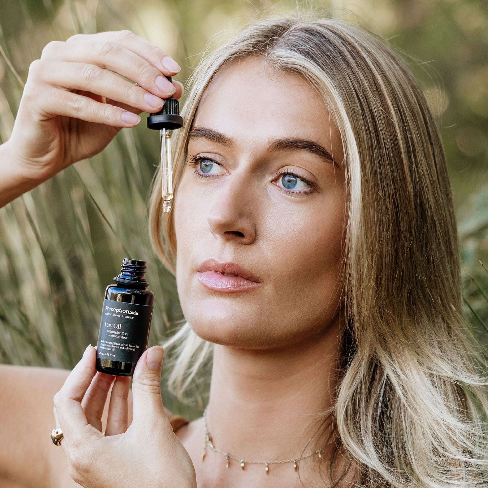 Model dropping Perception Skin's Watermelon Seed + Australian Rose Day oil on face in nature setting