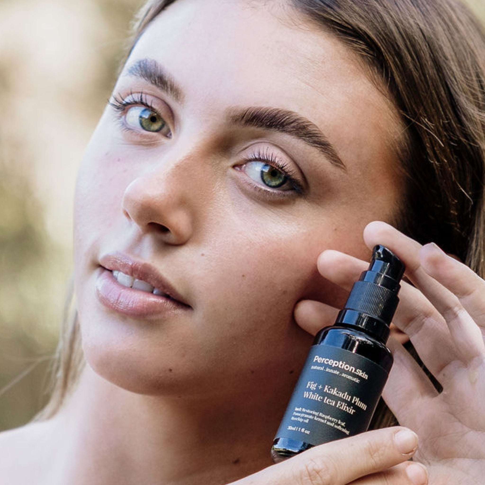 Model holding product close to face Perception Skin's Fig + Kakadu Plum White Tea Elixir