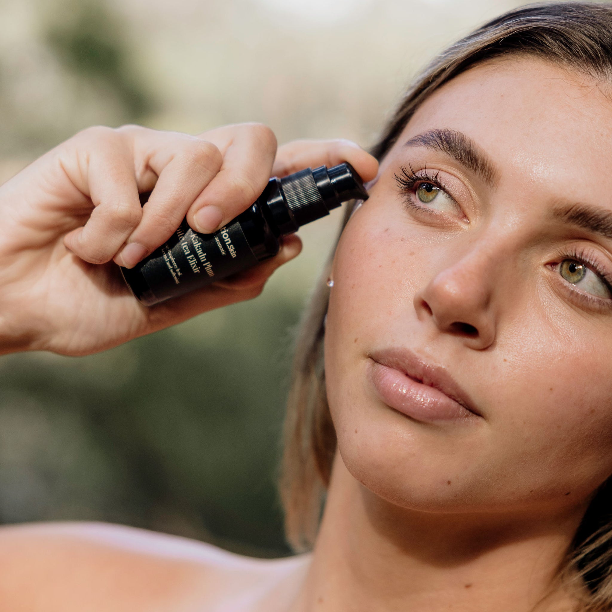 Model dropping Perception Skin's Fig + Kakadu White Tea Elixir on face in nature