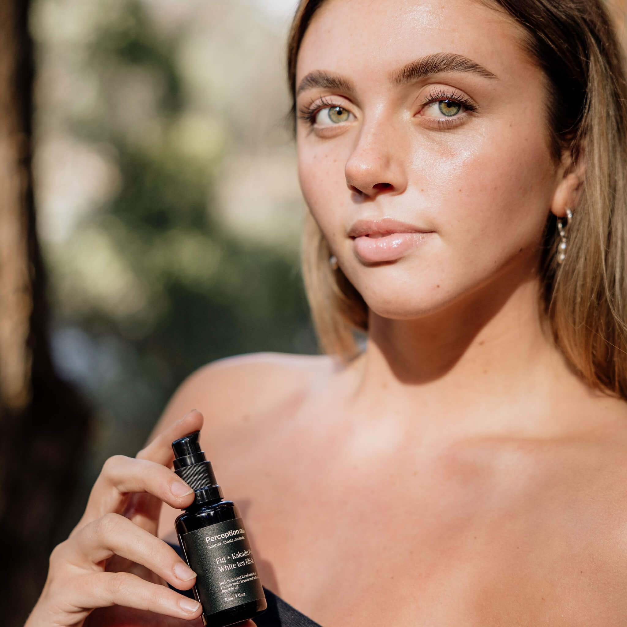 Woman holding a Perception skincare bottle outdoors with a blurred natural background