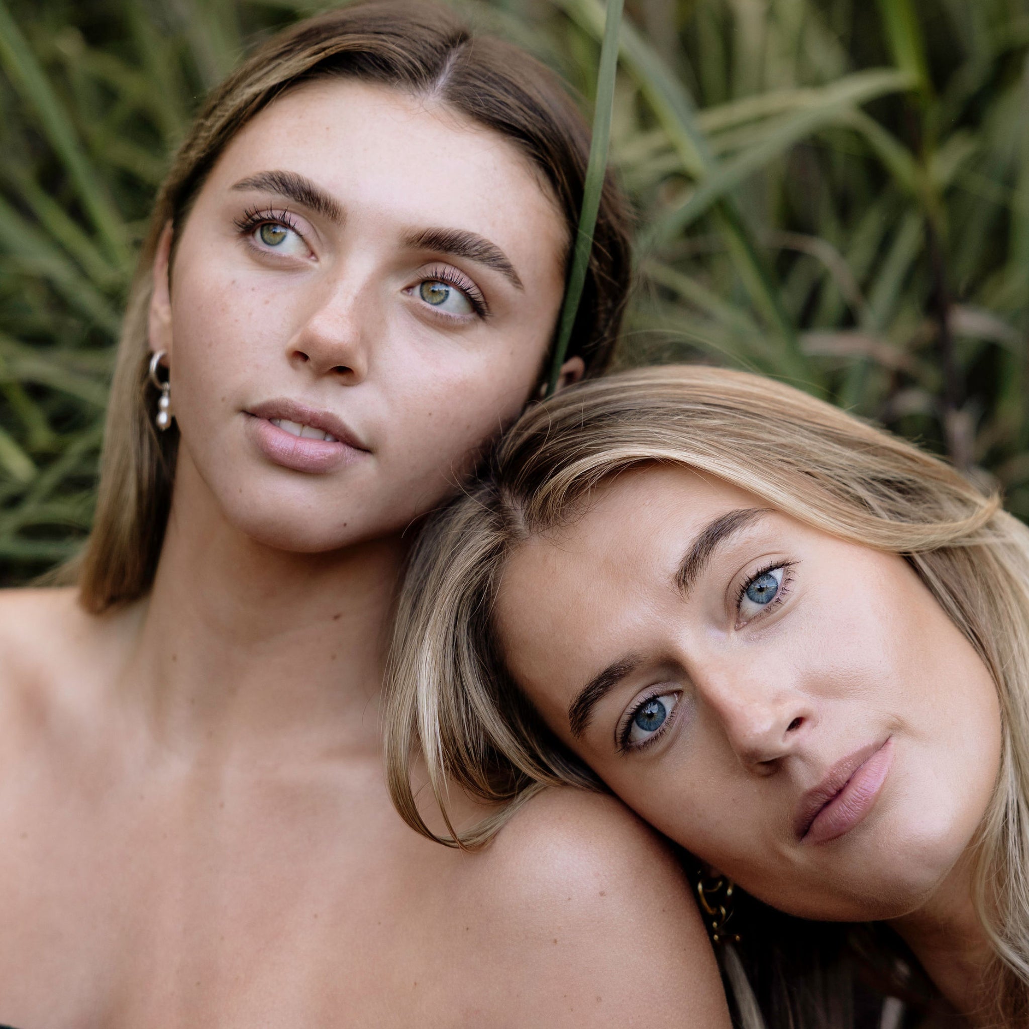 Two women posing closely together with a natural background