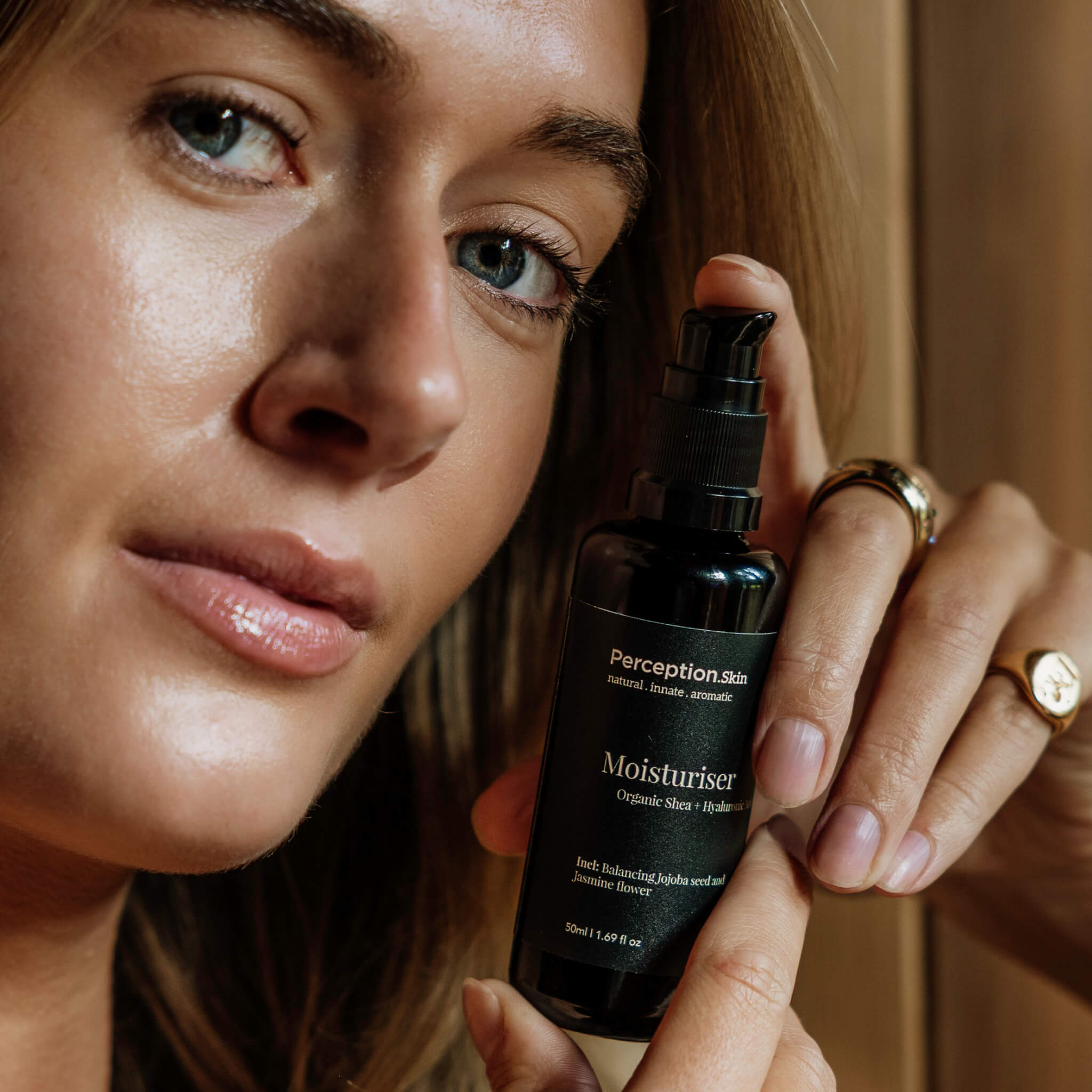 Woman holding a Perception Skincare moisturiser bottle close to her face.