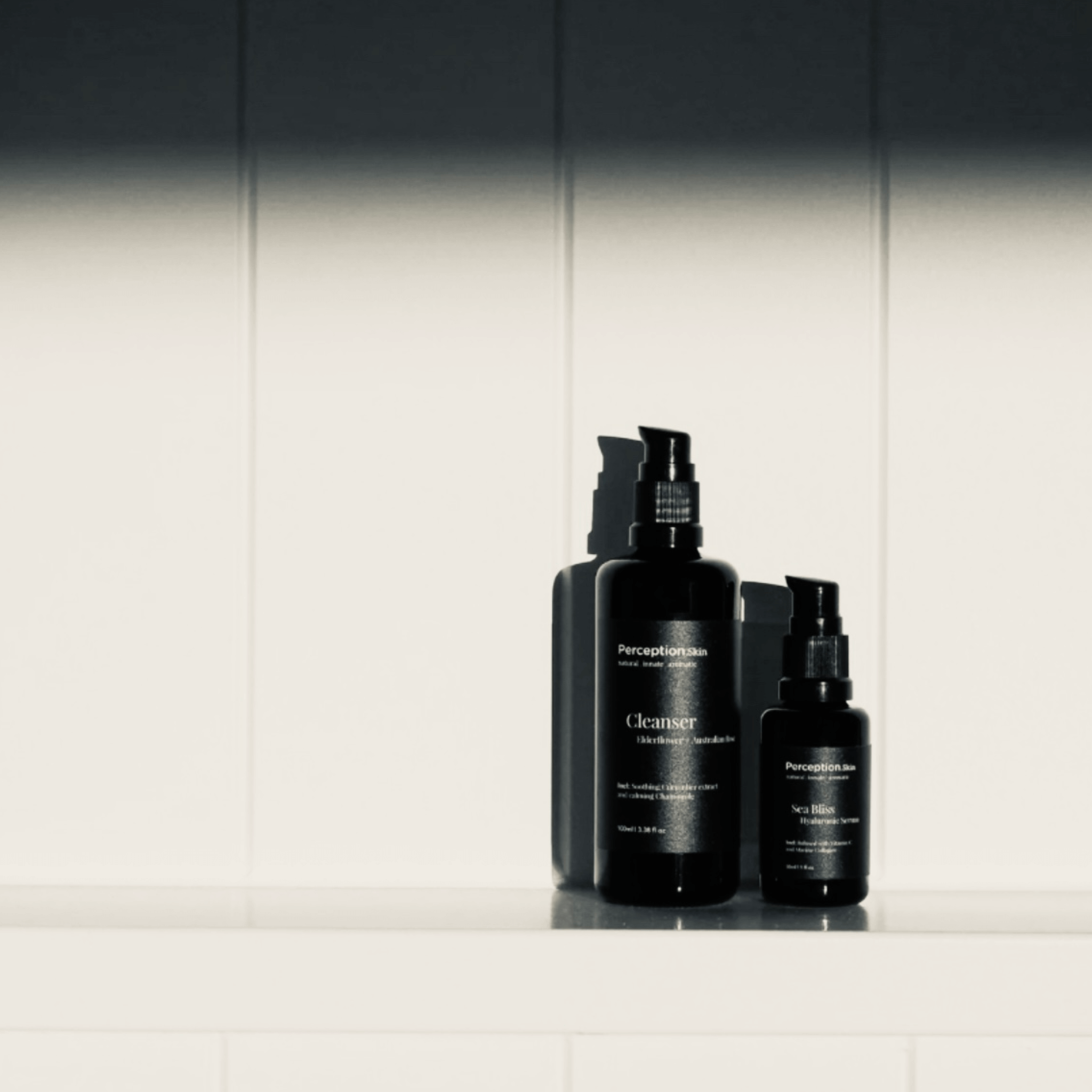 Two black Perception Skin skincare bottles on a white surface with a neutral background