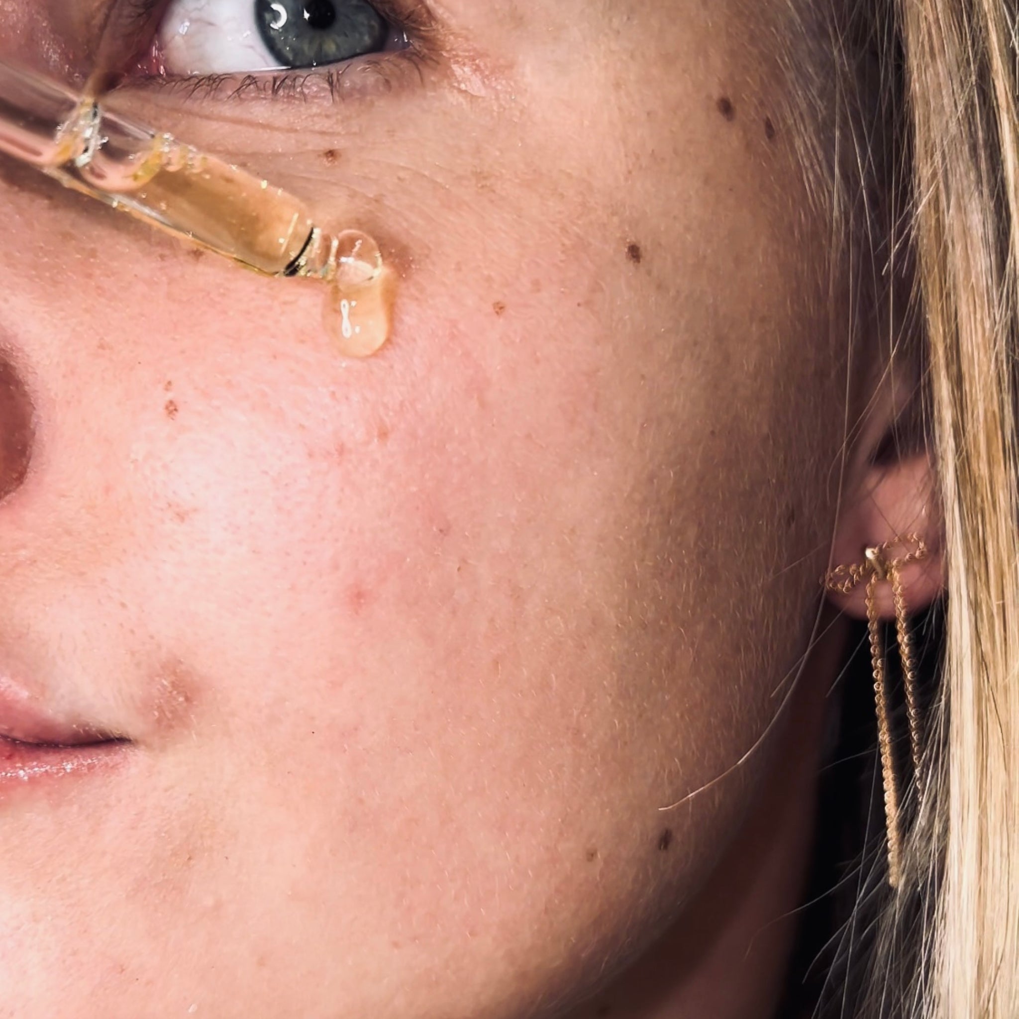 Close-up of a woman applying a dropper of skincare product to her face.