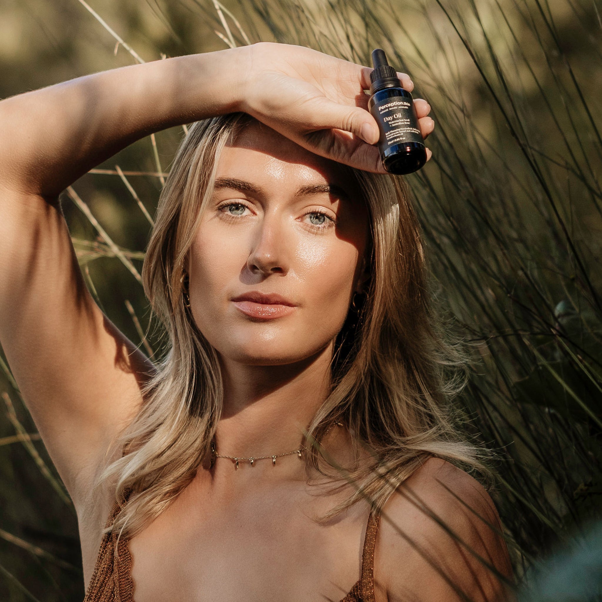Woman holding a dropper bottle of the Watermelon Seed + Australian Rose Perception Skin Day oil with a natural background