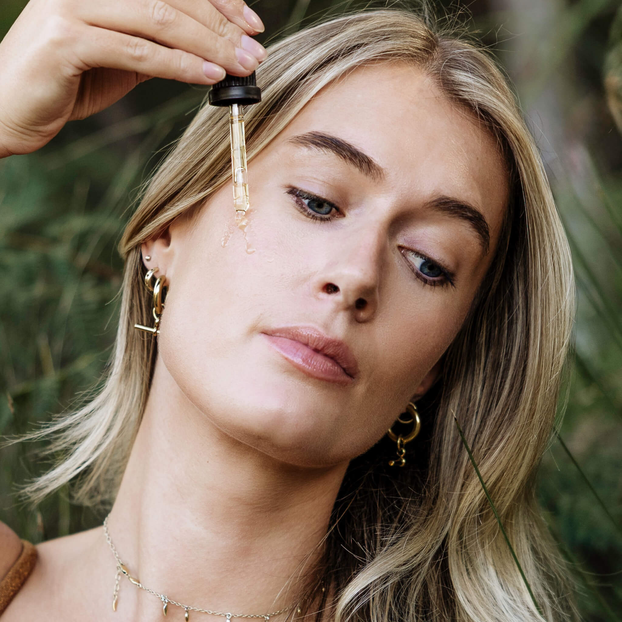 Woman applying a dropper of liquid to her face with a natural background