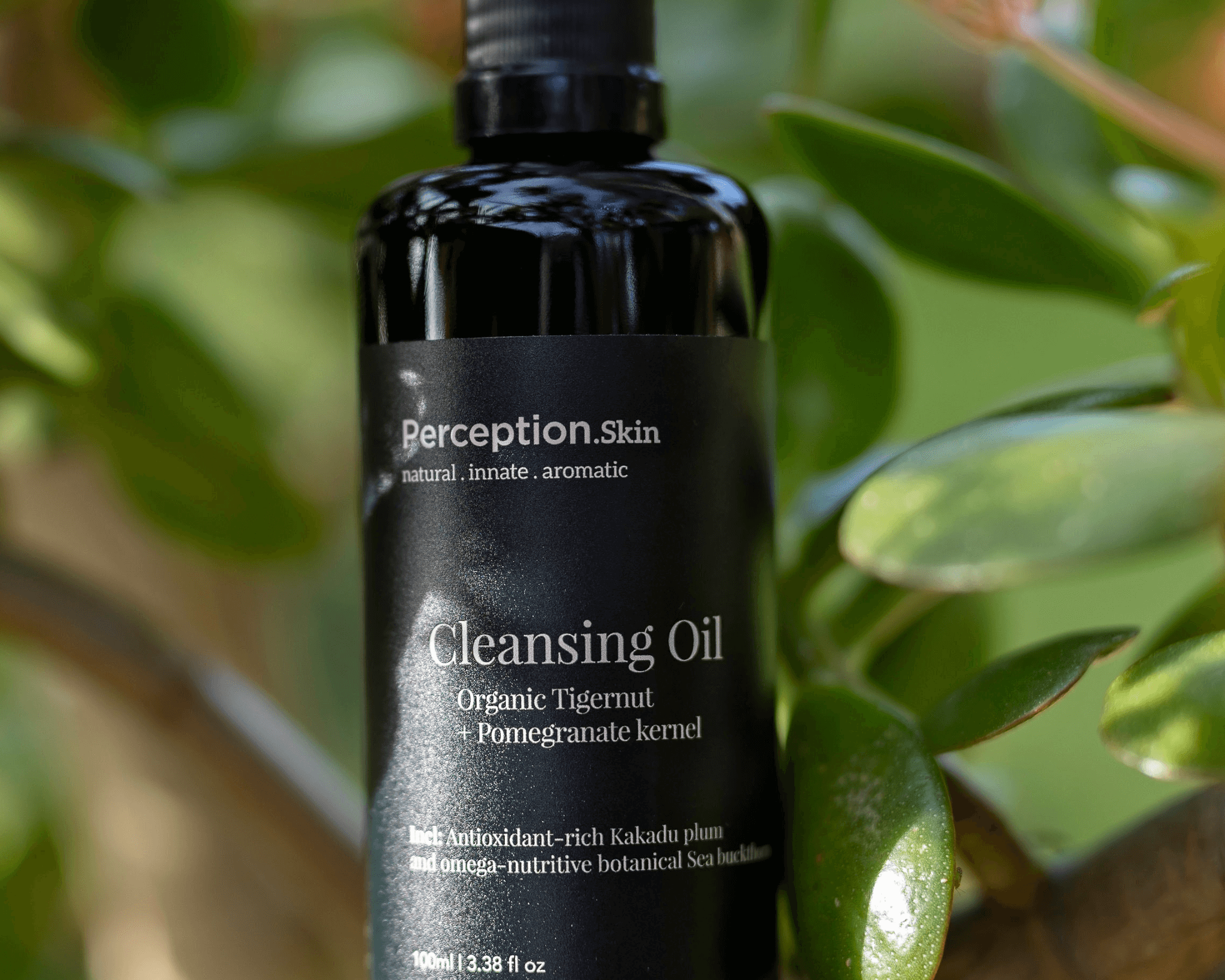 Black bottle of perception Skin Cleansing Oil with green leaves in the background