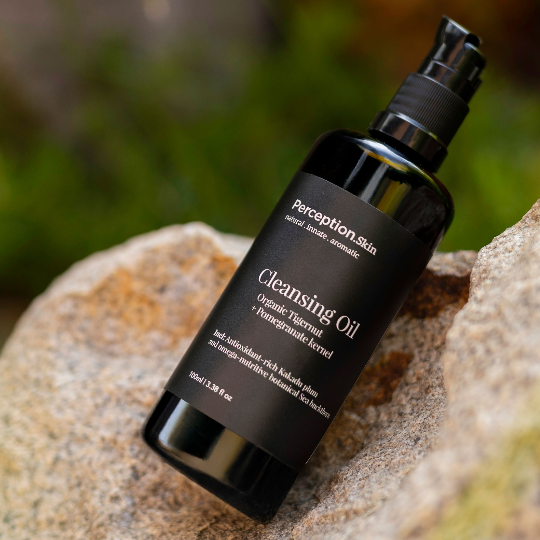 Black bottle of perception skincare cleansing oil on a rock with a blurred green background