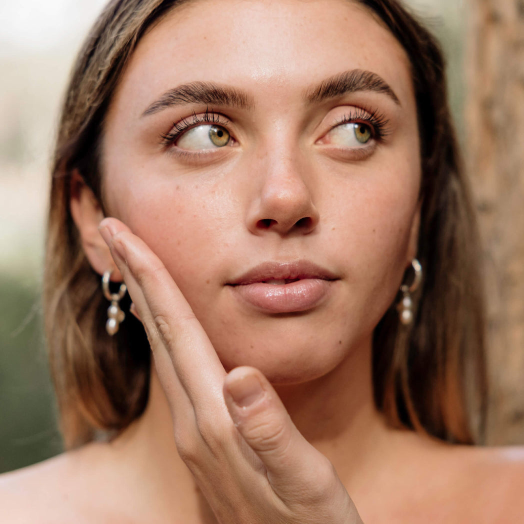 Woman with hand near face against a blurred natural background